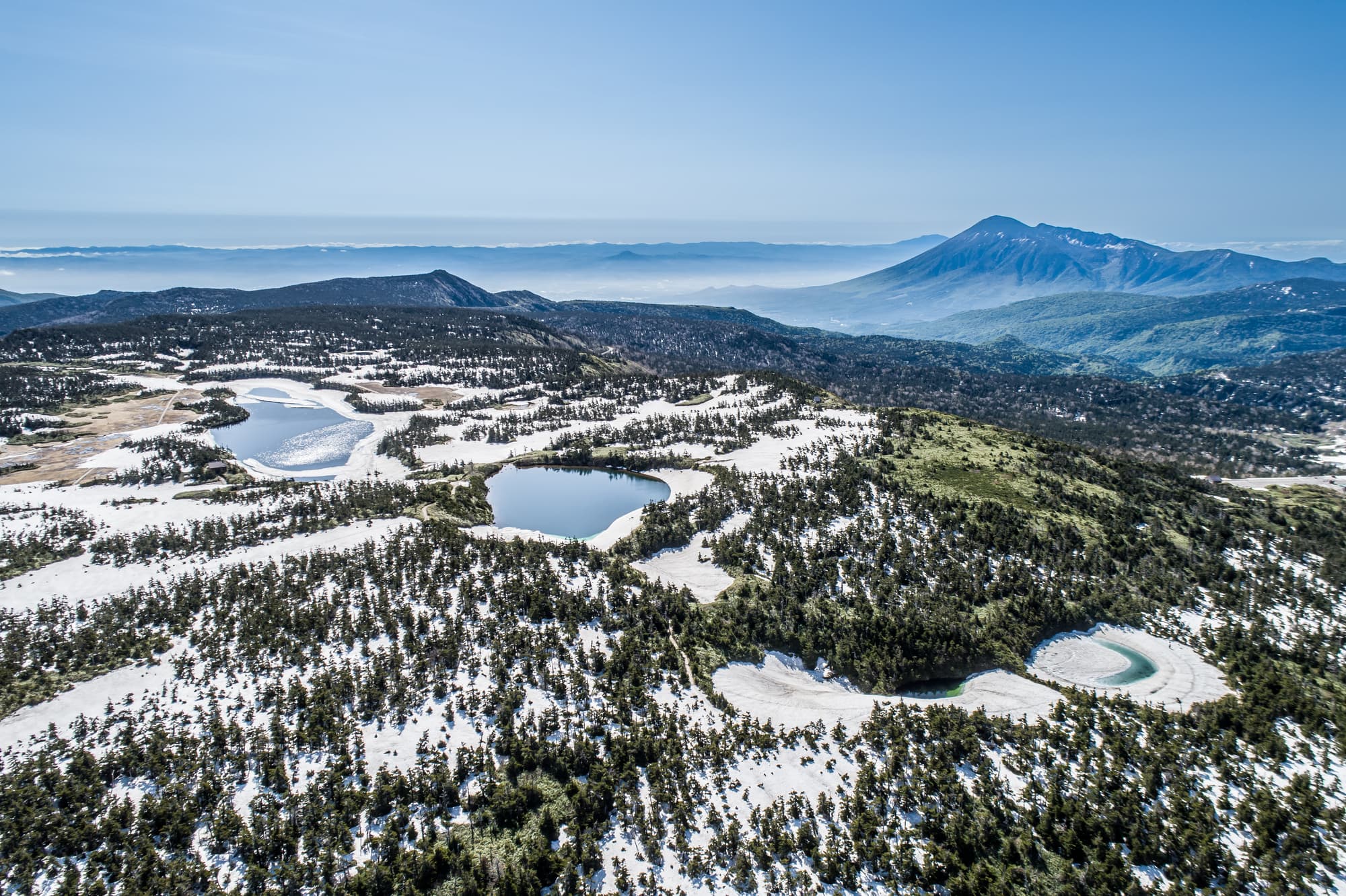 残雪の沼が点在する八幡平と岩手山の空撮