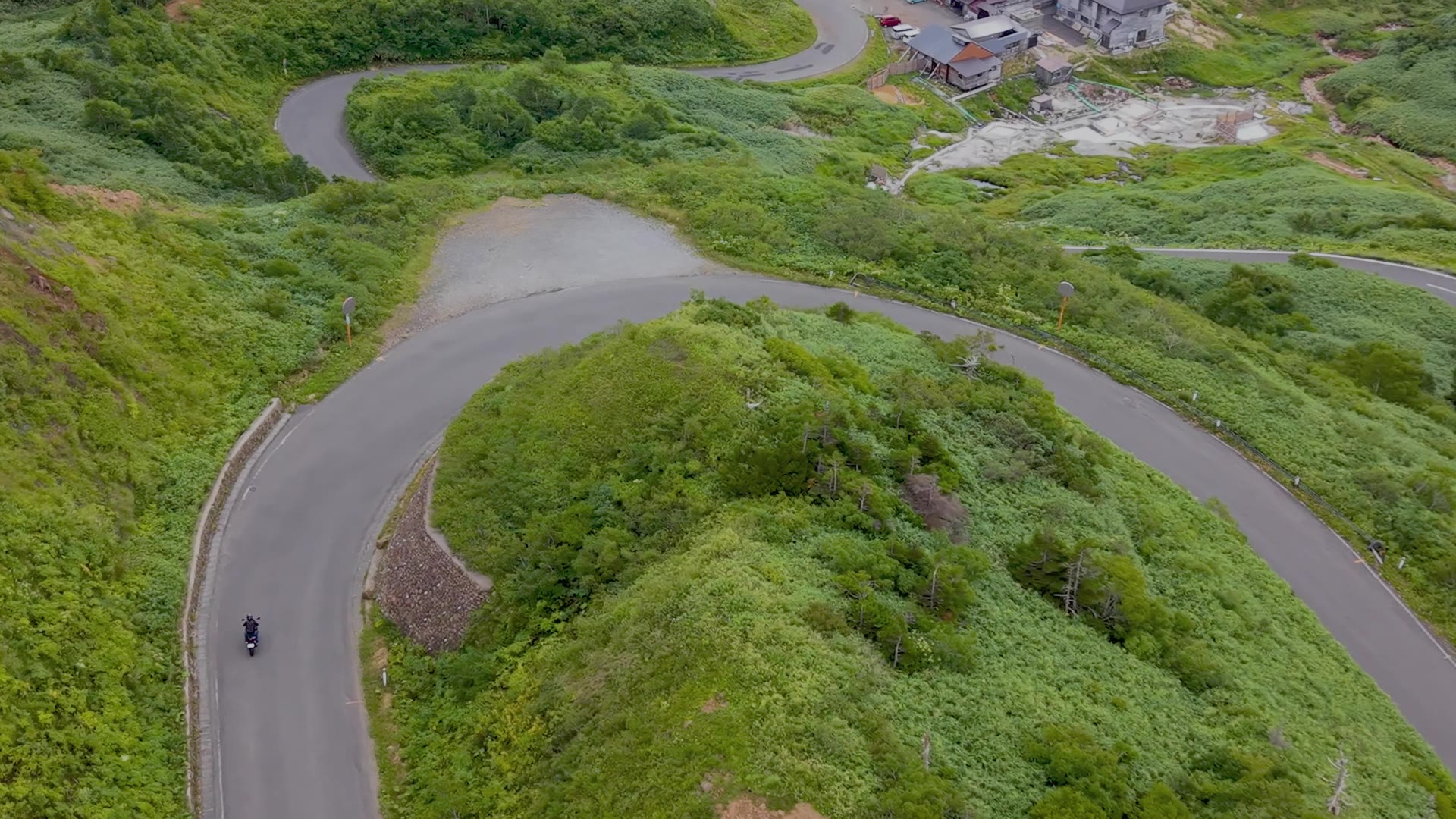 つづら折りの山道を走るバイクの空撮